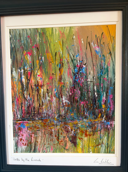 A framed abstract landscape painting depicting tall grasses and reeds with colorful brushstrokes of green, yellow, pink, orange, blue, and brown, presented in a black frame with a white mat.