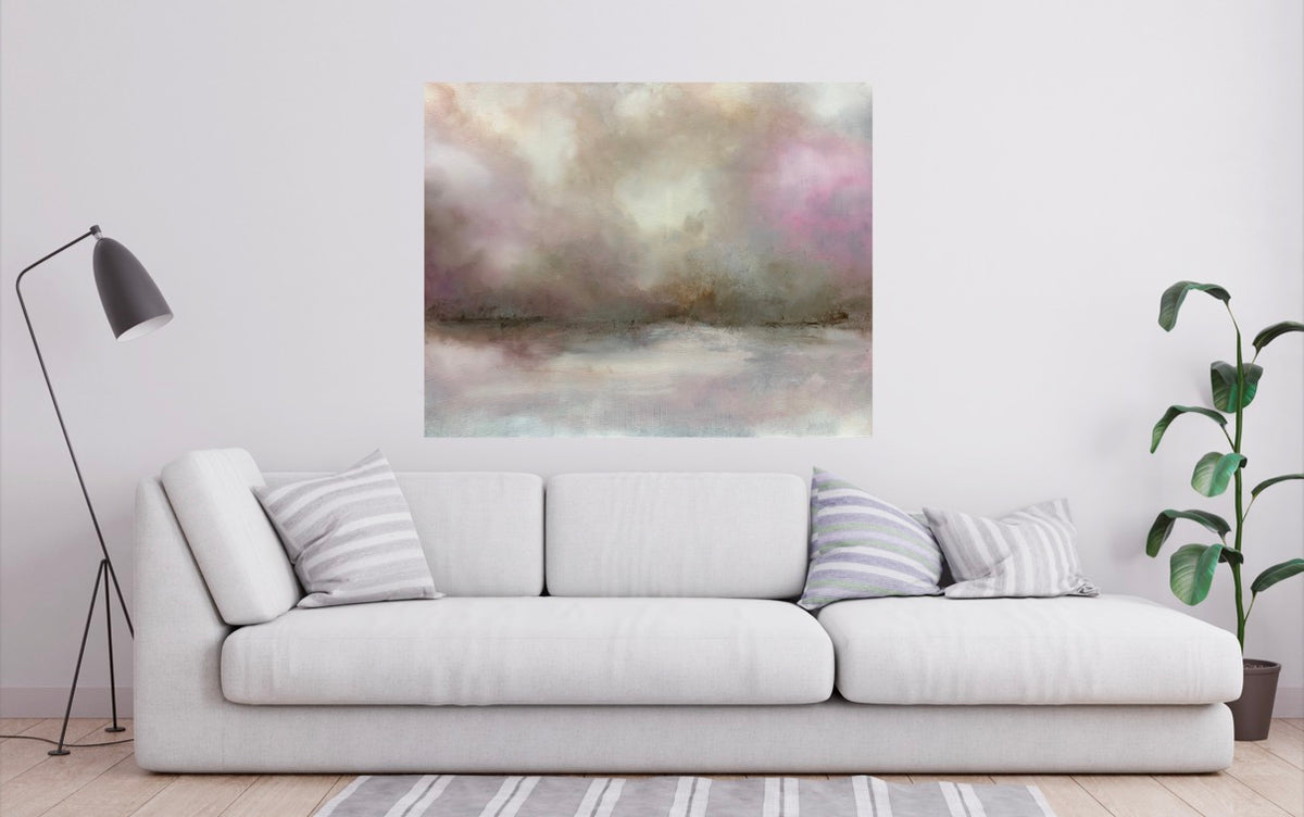 An abstract watercolor-style wall art print with soft pink, gray, beige, and muted blue tones, displayed above a white sofa in a modern living room setting.